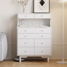 a white dresser sitting next to a lamp on top of a hard wood floor