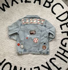 Custom Name or Saying Denim Sports Jacket. Such a fun addition to any Mom's wardrobe during sports season! Using Chenille lettering and patches each jacket is custom and unique. These various and unique patches will be in the chosen sports theme using either MAMA or Last Name specified on back. Jacket Brands are sourced upon size availability in light denim. All patches are adhered with high heat followed with hand stitching to ensure they will be secured. Last Name On Jean Jacket, Baseball Mom Jacket, Baseball Mom Jean Jacket, Baseball Jean Jacket, Letterman Jacket Ideas, Denim Patch Jacket, Baseball Fits, Cursive Embroidery, Letterman Patches