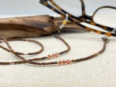 Shiny and bohemian eyeglass necklace chain in copper and gold tones, made with Preciosa Czech crystal seed beads and tiny Sunstone gemstone beads.    Paired with delicate copper plated Japanese Miyuki crystal seed beads and gold touches of the Sunstone gems, this handmade eyeglass chain will definitely create a unique look. Sunstone is linked to luck and good fortune. It instills good nature, heightens intuition and allows the real self to shine through happily. It alleviates stress and increase Adjustable Glass Gemstone Beads, Handmade Brown Glass Beads, Brown Glass Beads For Jewelry Making, Artisan Adjustable Glass Beads, Bohemian Brown Glass Beaded Necklaces, Brown Glass Beaded Necklaces As Gift, Brown Glass Beaded Necklaces For Gifts, Handmade Brown Glass Beaded Necklaces, Gold Bohemian Glass Beads