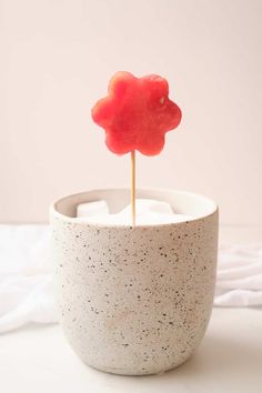 there is a small red candy on a stick in a white cup with black speckles