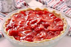 a pie with strawberries in it sitting on top of a table next to silverware