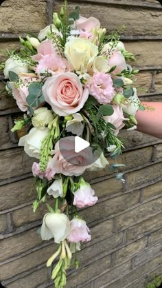 a bridal bouquet with pink and white flowers hanging on a brick wall in front of a woman's hand