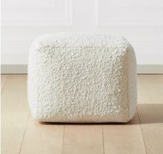 a white pouffle sitting on top of a wooden floor next to a wall