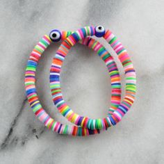 "Ward away nasty evilness with this super fun heishi bead bracelet with a woo-woo evil eye bead. + choose from three sizes: Small (6\"), Medium (6.75\"), or Large (7.5\") + 8mm blue glass evil eye bead + 6mm soft vinyl Heishi beads (random patterns vary) + clear stretch cord + this listing is for 1 (one) bracelet + to keep your jewelry looking new, avoid water, lotions and perfumes. NEED A CUSTOM SIZE? Just ask! I'm happy to accommodate custom requests. FREE DOMESTIC SHIPPING ABOUT THE MAKER Hi! Multicolor Novelty Wristband Bracelet, Multicolor Evil Eye Beaded Bracelets For Friendship, Adjustable Multicolor Novelty Wristband, Adjustable Multicolor Rave Stretch Bracelet, Multicolor Beaded Novelty Bracelets, Novelty Multicolor Festival Bracelets, Novelty Multicolor Beaded Festival Bracelets, Multicolor Novelty Beaded Bracelets For Festivals, Novelty Multicolor Bracelets For Festival