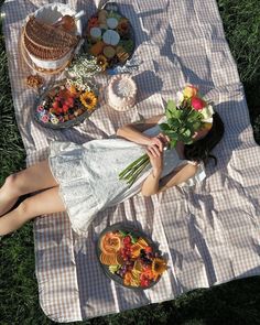 a woman is laying on the grass with food and flowers in her hand while she eats