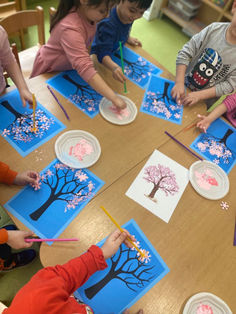 children are sitting at a table making paper plates with trees and flowers painted on them