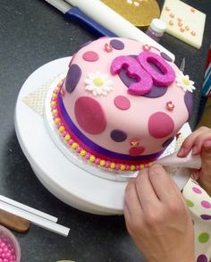 a woman is decorating a pink cake with polka dots and the number 50 on it