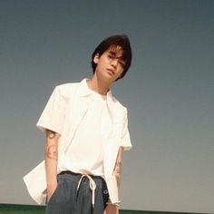 a man standing on top of a beach next to the ocean with his hands in his pockets