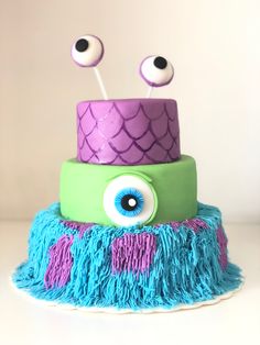 a three tiered cake decorated with blue and green frosting, purple icing and two eyeballs on top