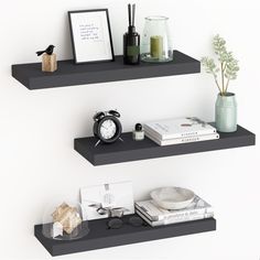 two black floating shelves with books, vases and other items on them in front of a white wall