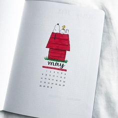 an open notebook with a drawing of a doghouse on the front and calendar in the back