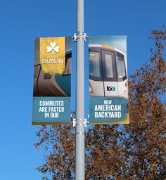 two banners on a street pole with trees in the back ground and blue sky behind them