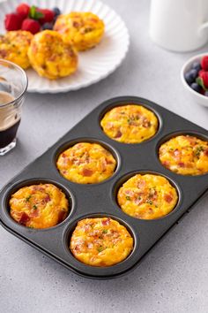 some muffins in a pan on a table next to berries and coffee cup