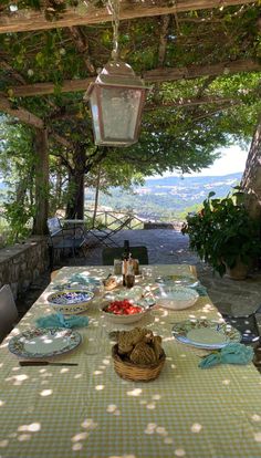 an outdoor table with plates and food on it under a pergolated roof over looking the countryside