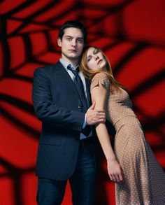 a man and woman standing next to each other in front of a red background,