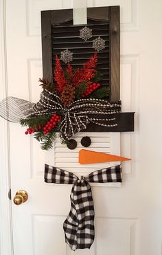 a snowman door hanger decorated with red berries and pine cones