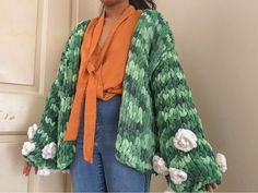 a woman standing in front of a door wearing a green and white jacket with flowers on it