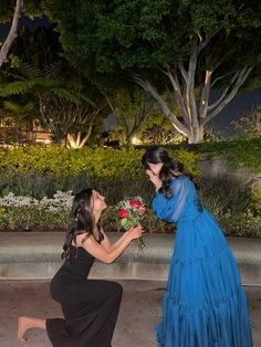 two women in dresses kneeling down to give each other flowers