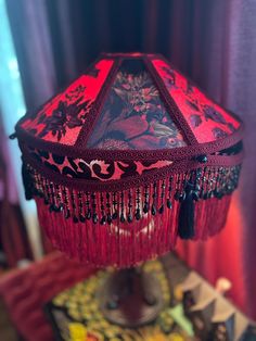 a red and black lamp with tassels hanging from it's sides on a table