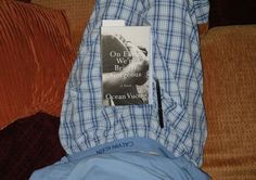 an open book laying on top of a bed next to a blue and white checkered shirt