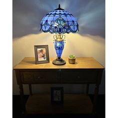 a blue lamp sitting on top of a wooden table next to a framed photo and potted plant