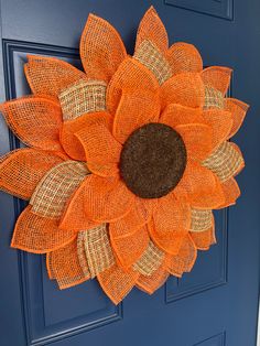 an orange mesh sunflower on a blue front door with burlap and jute