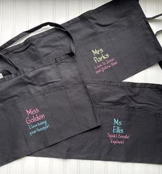 three black aprons with embroidered words on them