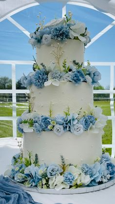 a wedding cake with blue and white flowers on it sitting in front of a window