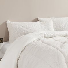 a bed with white comforter and pillows on top of it next to a night stand