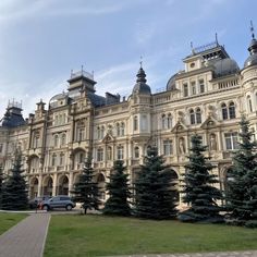 a large building with many trees in front of it and a car parked on the side