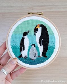 a hand holding a small cross stitched penguin with its chickling on it's belly