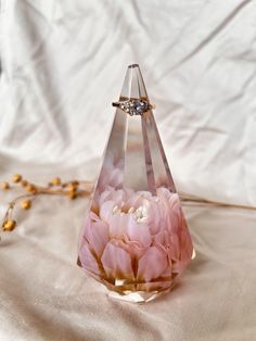 a glass vase with flowers in it sitting on a white cloth covered tablecloth next to a gold ring