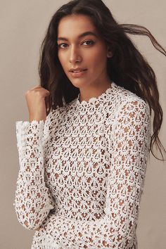 a woman wearing a white crochet top poses for the camera with her hair blowing in the wind