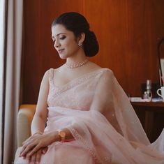 a woman in a pink sari sitting on a chair with her hand on her knee