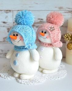 two snowmen are sitting on a doily next to a candle and some flowers