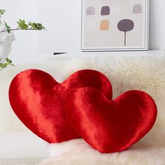 two red heart shaped pillows sitting on top of a white couch