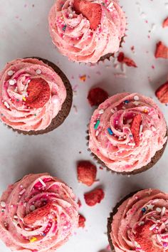 several cupcakes with pink frosting and sprinkles on a white surface