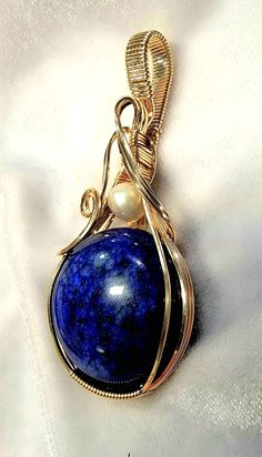 This beautiful Lapis gemstone with an Akoya Pearl accent is artfully hand wire wrapped in 14K (14/20) gold filled wire.  The pendant measures 2 3/8 inches in length and is 1 1/8 inch wide.  The bail is generously sized in order to accommodate a variety of chain widths. A handcrafted pendant and a beautiful Lapis and Pearl,  it is one of a kind. A gift box is included. Note of Interest: Wire wrapping can be traced back to several ancient civilizations such as the Vikings, Celts, and the Egyptians.  Some believed that wire-wrapped jewelry had magical and spiritual properties and it was used in many rituals and ceremonies, particularly with the Celts. Lapis And Pearl, The Celts, The Vikings, Akoya Pearls, Wrapped Jewelry, Ancient Civilizations, Pearl Pendant, Wire Wrapped Jewelry, Wire Wrapped