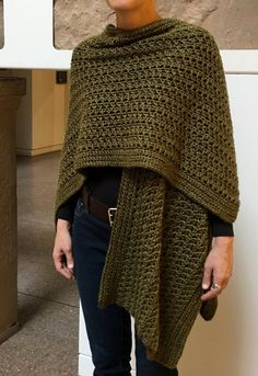 a woman standing in front of a wall wearing a green knitted ponchy