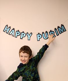 a young boy is holding up a happy purim banner in front of him and smiling at the camera