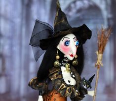 a doll dressed as a witch holding a broom and wearing a black hat with gold accents