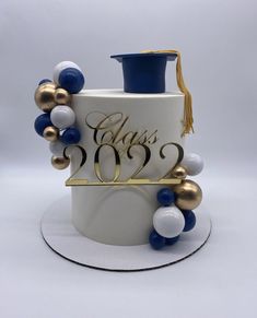 a white cake with gold and blue decorations on it's side, topped with a graduation cap