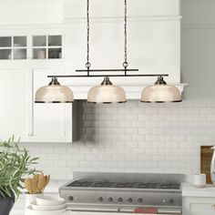 three lights hanging over a stove top in a kitchen next to a potted plant