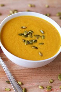 a white bowl filled with carrot soup and topped with pumpkin seeds next to a spoon