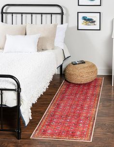 a bedroom with white walls and wood flooring has a red rug on the floor