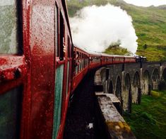 a red train traveling over a bridge on top of a lush green hillside covered in fog