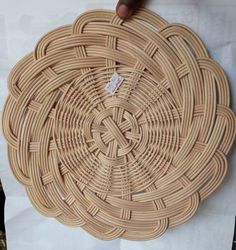 a person is holding up a woven piece of art that looks like a circular basket