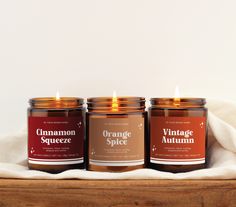 three orange spice candles sitting on top of a wooden table next to a white towel