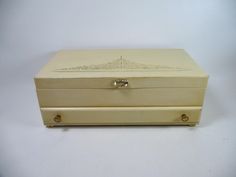 a white wooden box with an ornate design on the lid and handles, sitting on a plain surface