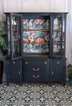 an antique china cabinet with floral wallpaper on the back and gold trimmings